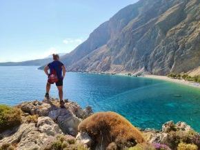 On a coastal hike, Chrissy Elliott stands with her back to the camera overlooking the Loutro Bay in Crete, 希腊.